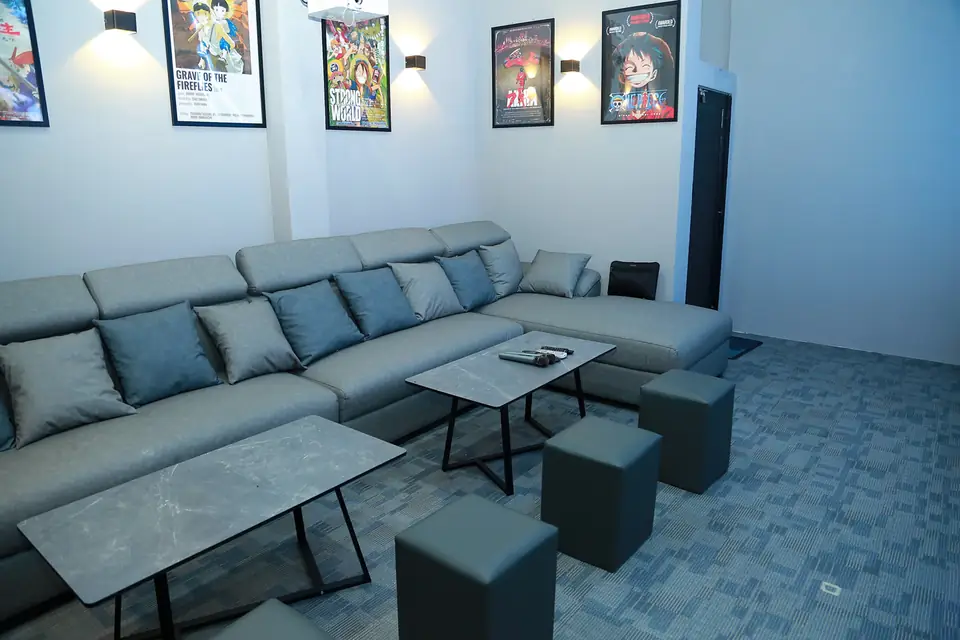 Sala svago con divano grigio, pouf quadrati e poster anime incorniciati, casa con karaoke a Ho Chi Minh